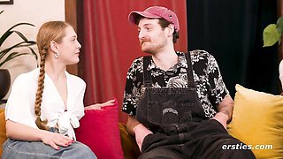 Two women kiss naked while man watches from behind plants